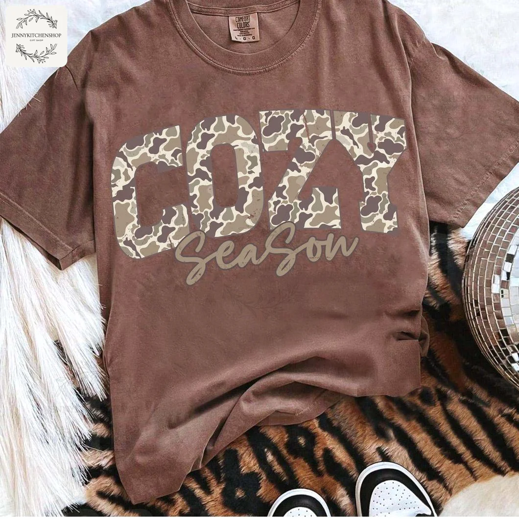 Brown Cozy Season Camo Western T-Shirt Flat Lay A flat lay of the brown Cozy Season Camo T-Shirt styled on a tiger-print rug with a disco ball and pampas grass.