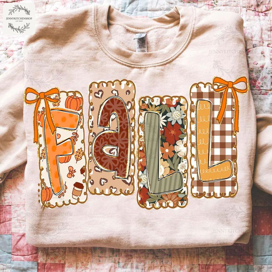 A beige sweatshirt with the word FALL in decorative letters with pumpkin, leopard, floral, and plaid patterns on a quilt.
