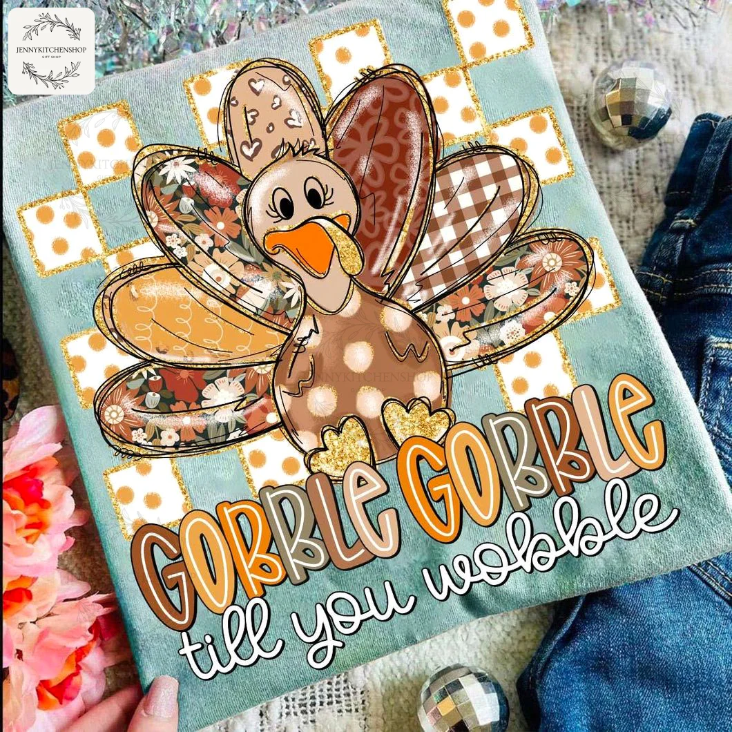 A light blue Thanksgiving t-shirt featuring a patchwork turkey and "Gobble Gobble till you wobble" text, styled in a flatlay.