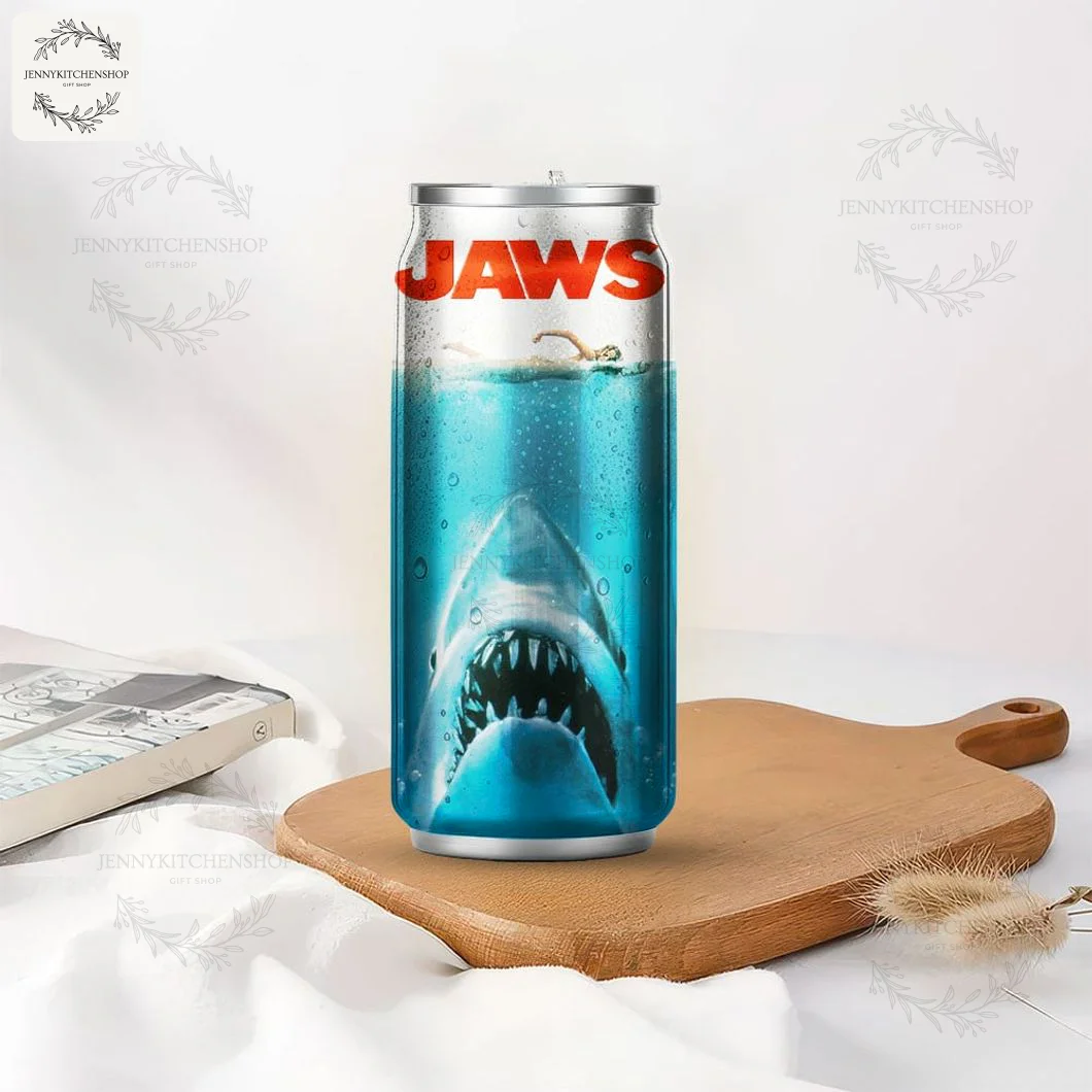 Jaws 50 Years Premium Can Shaped Tumbler in a Lifestyle Setting The Jaws 50 Years can tumbler with the classic shark poster design, sitting on a wooden board next to a book.