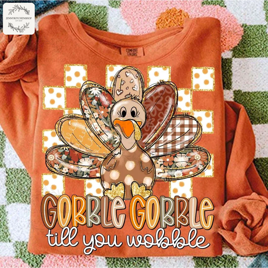 "Gobble Till You Wobble" Thanksgiving Long-Sleeve Shirt An orange long-sleeve Thanksgiving shirt laid flat, featuring a cute cartoon turkey with patchwork feathers and fun text.