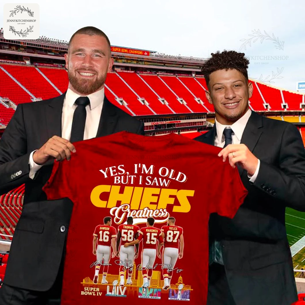 Two people in suits holding a red "Yes, I'm Old But I Saw CHIEFS Greatness" T-shirt inside a Kansas City Chiefs stadium, front print visible with four players' backs (Dawson 16, Thomas 58, Mahomes 15, Kelce 87) and Super Bowl icons